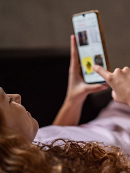 Eine junge Frau liegt auf dem Sofa und schaut auf ihr Smartphone.