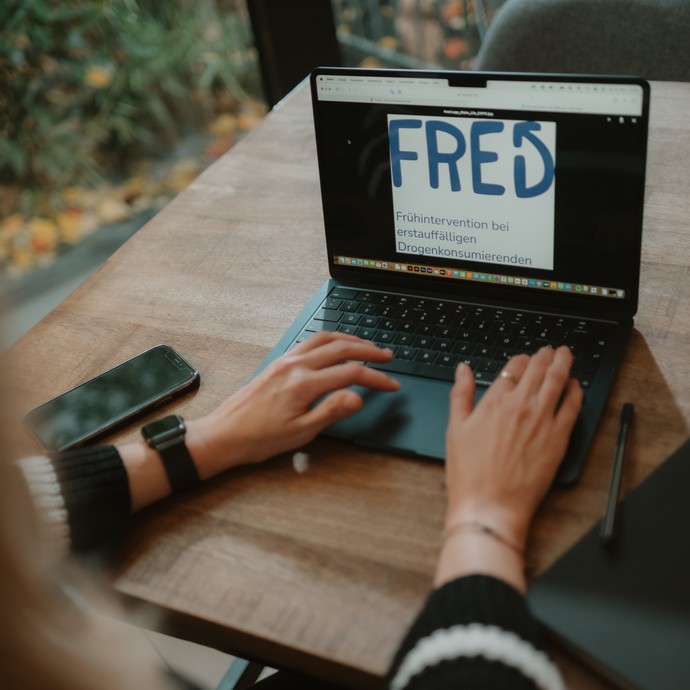 Person sitzt am Laptop, auf dem Bildschirm ist das FreD Logo abgebildet (vergrößerte Bildansicht wird geöffnet)